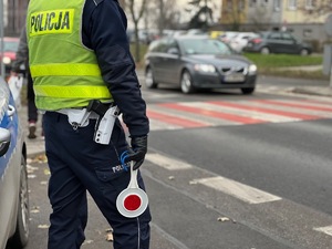 zdjęcie poglądowe policjanta stojącego przy przejściu dal pieszych, które przejeżdża samochód