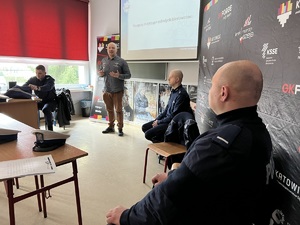 zdjęcie w klasie lekcyjnej przedstawiające kierowcę rajdowego i policjantów w trakcie prelekcji