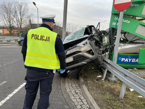 zdjęcie z miejsca wypadku przedstawia policjanta z drogówki stojącego przed rozbitym samochodem