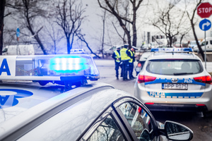 zdjęcie poglądowe, policyjne radiowozy i czarny samochód na ulicy w tle zabudowania