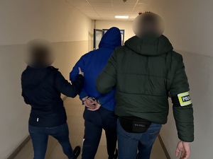 zdjęcie - policjanci kryminalny z zatrzymanym w kajdankach idą korytarzem