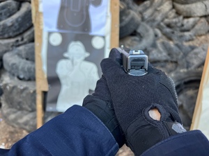 zdjęcie z treningu strzeleckiego - ręce policjanta trzymające pistolet, w tle tarcze strzeleckie