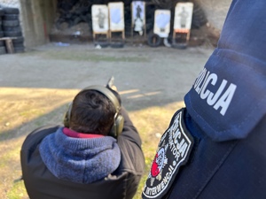 zdjęcie z treningu strzeleckiego - policjant w cywilu strzelający z pozycji klęczącej, obok stoi instruktor