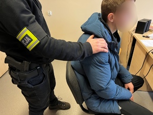 zdjęcie - policjant stojący przy siedzącym zatrzymanym w trakcie przesłuchania