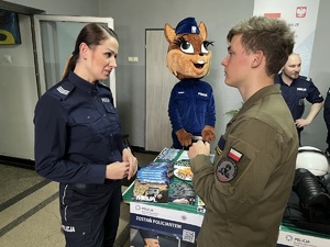 zdjęcie - policjantka z wydziału doboru rozmawia z uczniem w mundurze w tle sierżant ruda, maskotka policji