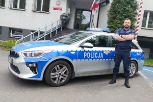 Policjant stojący przy radiowozie na tle Komendy Miejskiej Policji w Rudzie Śląskiej