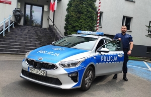 Policjant stojący przy radiowozie na tle Komendy Miejskiej Policji w Rudzie Śląskiej