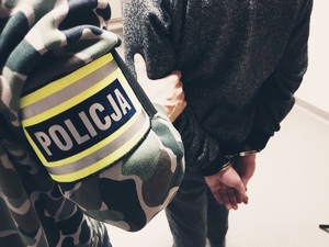 zdjęcie poglądowe przedstawiające policjanta kryminalnego z opaską &quot;policja&quot; wraz z zatrzymanym zakutym w kajdanki