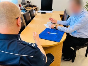 zdjęcie ze spotkania - policjant z mężczyzną siedzą przy stoliku, na którym leżą otrzymane upominki