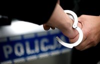 zdjęcie - radiowóz policyjny, ręce i zakładane kajdanki