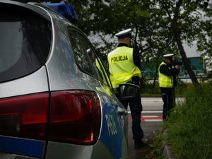zdjęcie z działań prędkość - dwaj policjanci z drogówki stojący przy drodze przed radiowozem