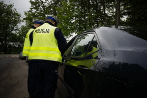 zdjęcie z działań prędkość - dwaj policjanci stojący przy samochodzie którego kierowca przekroczył prędkość