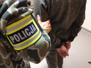 zdjęcie poglądowe, policjant kryminalny z opaską prowadzi zatrzymanego