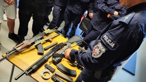 zdjęcie - policyjny instruktor pokazuje ułożoną na stoliku broń palną będącą na wyposażeniu policji