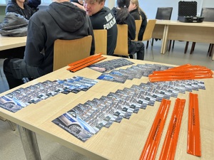 zdjęcie - ustawiony na środku sali stolik z ulotkami dotyczącymi rekrutacji i odblaskowymi opaskami w kolorze pomarańczowym