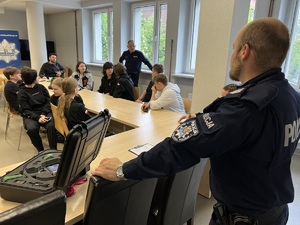zdjęcie - zebrani słuchają opowieści policjanta o jego pracy, drugi stoi przy stoliku