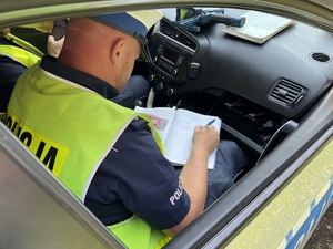 zdjęcie - policjant z drogówki w radiowozie wypełnia dokumentację dotyczącą kontroli drogowej