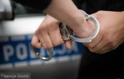 zdjęcie poglądowe - drzwi policyjnego radiowozu, ręce policjanta i zatrzymanego w kajdankach