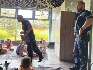 zdjęcie z sali wypoczynku parku wodnego, gdzie zebrane były dzieci w trakcie spotkania z policjantami - policjant po zadanym pytaniu czeka na odpowiedź