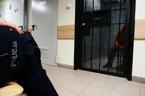 zdjęcie poglądowe - policjant siedzący przed celą w której jest zatrzymany - archiwum foto