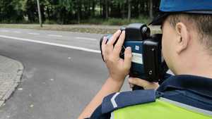 Policjant w trakcie prowadzonej kontroli prędkości, w rękach trzyma miernik prędkości.