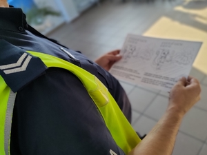 zdjęcie z wizyty policjantów w szkole - ramię policjanta trzymającego kolorowankę w rękach