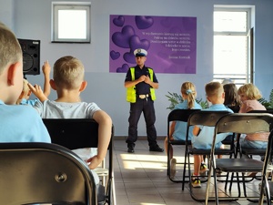 zdjęcie z wizyty policjantów w szkole - klasa z dziećmi i policjant stojący przed ławkami