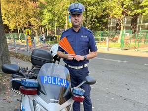 zdjęcie - policjant z drogówki w rejonie przejścia przy szkole, trzyma w rękach odblaski