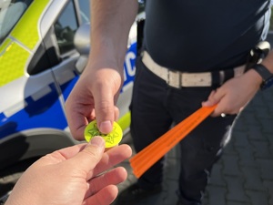 zdjęcie - policjant z drogówki, trzyma w rękach odblaski, które przekazuje innej osobie