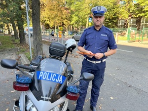 zdjęcie - policjant z drogówki w rejonie przejścia przy szkole, trzyma w rękach odblaski