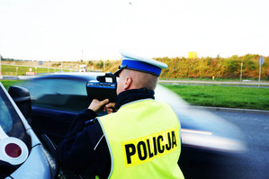 zdjęcie policjanta przy radiowozie w trakcie pomiaru prędkości ręcznym miernikiem