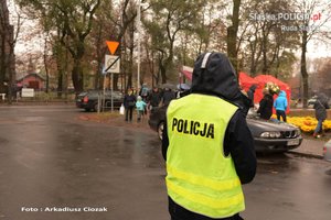 zdjęcie policjanta przed cmentarzem, widoczni ludzie, kwiaty samochody