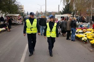 zdjęcie archiwalne, policjanci idący ulicą przy której po obu bokach widać stoiska z kwiatami