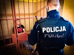 zdjęcie poglądowe z archiwum - policjant stojący przed celą w której siedzi zatrzymany mężczyzna