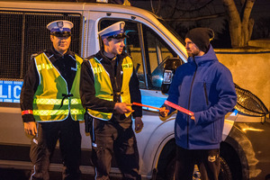 zdjęcie archiwalne - policjanci na tle radiowozu wieczorową porą przekazują odblaski mężczyźnie