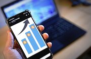 zdjęcie poglądowe - smartfon z grafiką słupków giełdowych i w tle komputer