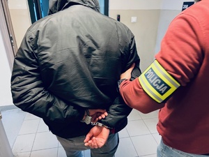 zdjęcie przedstawiające policjanta prowadzącego mężczyznę z kajdankami na rękach