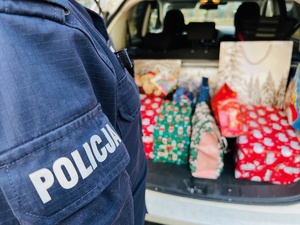 zdjęcie przedstawia policjanta stojącego przy samochodzie z prezentami
