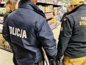 zdjęcie z kontroli miejsc sprzedaży fajerwerków - policjant i strażak stoją przed alejką z wyrobami pirotechnicznymi