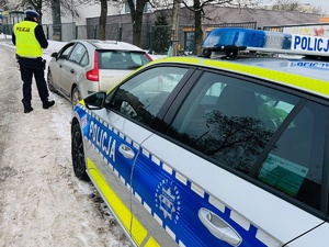 zdjęcie przedstawia radiowóz policyjny i stojący przed nim samochód osobowy, policjant rozmawia z kierowca stojąc przy osobówce
