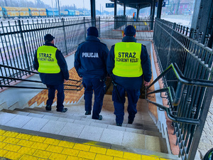 zdjęcie przedstawia policjanta i sokistów schodzących z peronu do dworcowego przejścia podziemnego