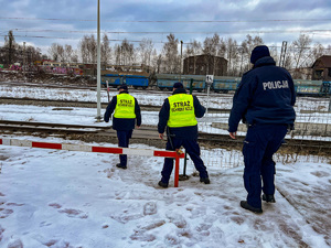 zdjęcie przedstawia policjanta i sokistów przechodzących przez techniczne przejście na torowisko