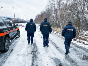 zdjęcie przedstawia policjanta i sokistów idących wzdłuż bocznicy kolejowej