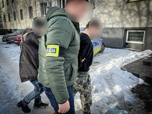 zdjęcie przedstawia policjantów prowadzących zatrzymanego z parkingu do budynku komendy