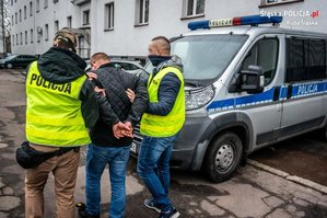 zdjęcie archiwalne - policjanci prowadzą zatrzymanego, w tle radiowóz policyjny i budynek komendy
