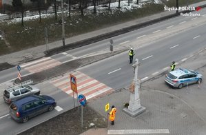 zdjęcie archiwalne - widok z góry na przejście dla pieszych, przed którym stoją dwa samochody i policjant nakazujący jednemu z nich zatrzymanie