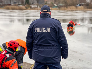zdjęcie przedstawia policjanta i strażaków przy zamarzniętym zbiorniku wodnym