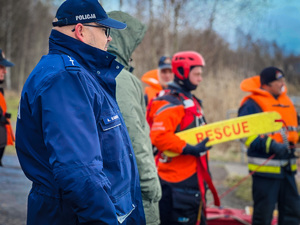 zdjęcie przedstawia policjanta przyglądającemu się pokazowi zakładania pasa ratunkowego