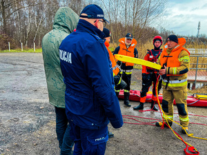 zdjęcie przedstawia policjantów i strażaków demonstrujących metodę ratowania ludzi z pod lodu