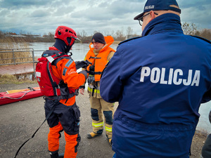 zdjęcie przedstawia strażaków pokazujących specjalistyczny sprzęt do ratownictwa wodnego, przygląda się temu policjant